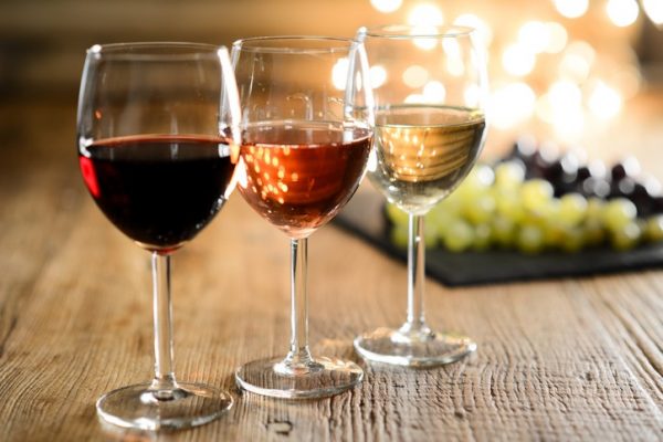 three glass of white red and rose wine with dim light in wooden restaurant table with a grape background three glass of white red and rose wine with dim light in wooden restaurant table with a grape background